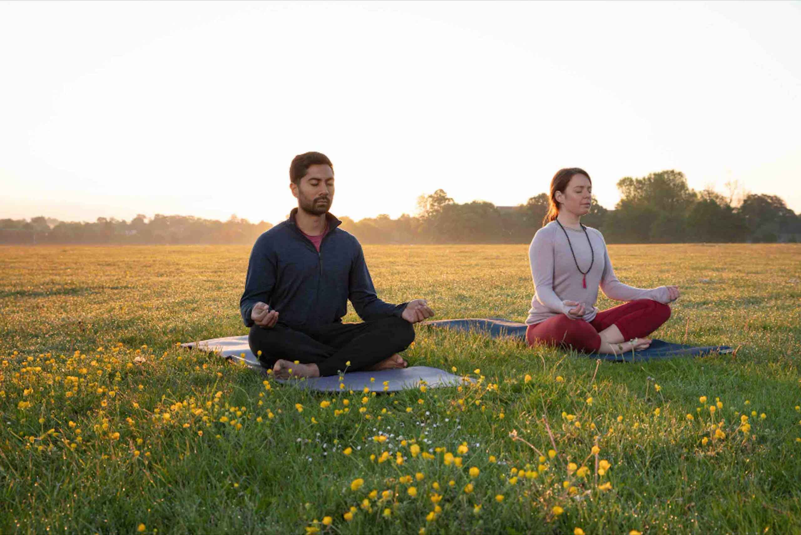 Man and woman doing yoga or breathing exercises together in a serene, calm natural environment